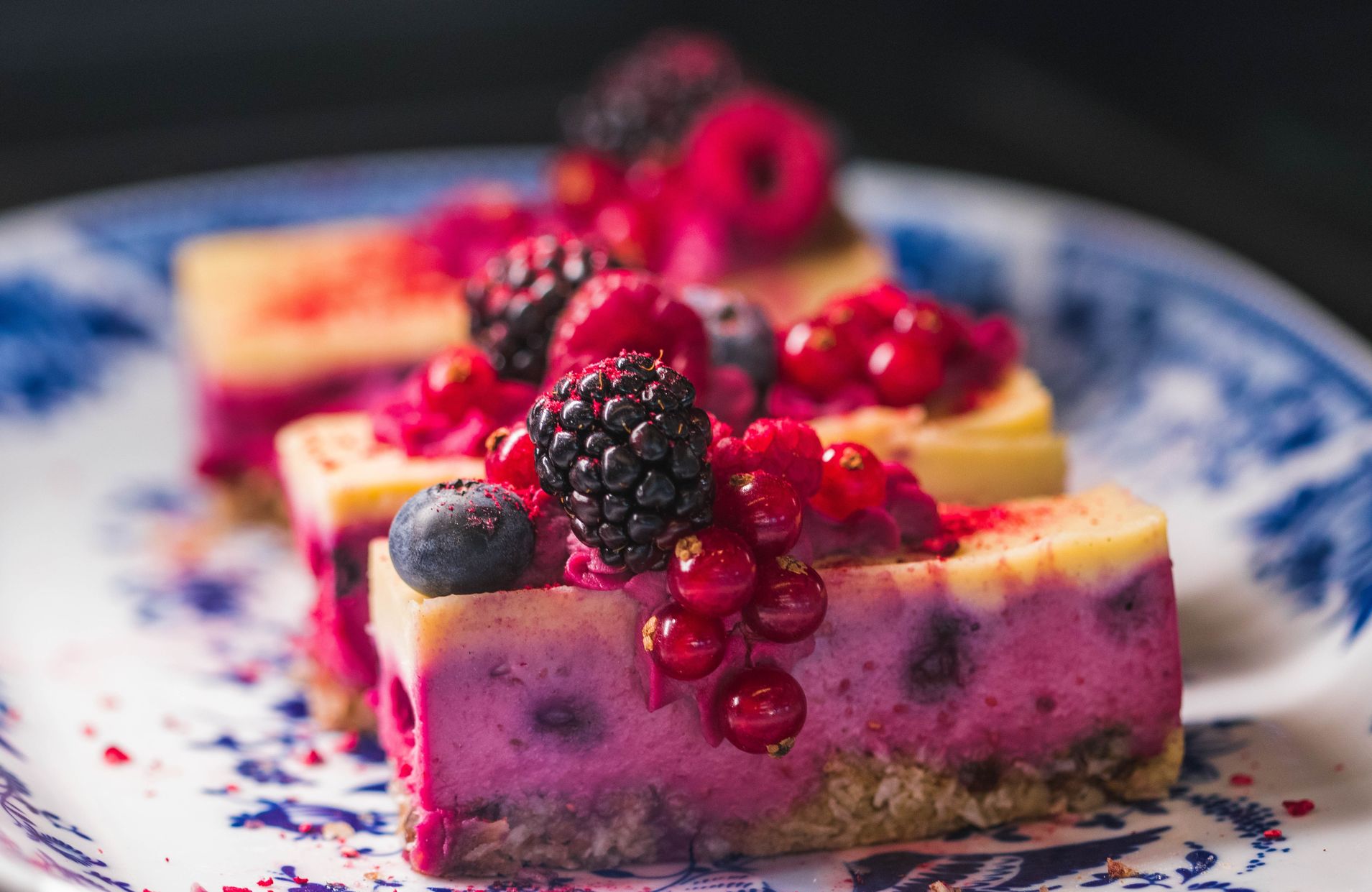 Image of a pink and yellow cake slice with blue and red berries on top on a white and blue plate